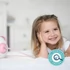 Bild 6/10 - Mosolygós kislány az ágyon könyököl, mellette Pink Nosiboo pro elektromos orrszívó