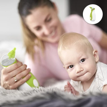 A cute, little boy sitting on the bed, holding the Nosiboo Go Portable Nasal Aspirator in his hands